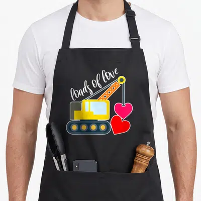 Toddler valentine's day apron - Yellow crane lifting pink heart, red heart on ground, loads of love text in white script — shown on a black cotton canvas apron against a white background