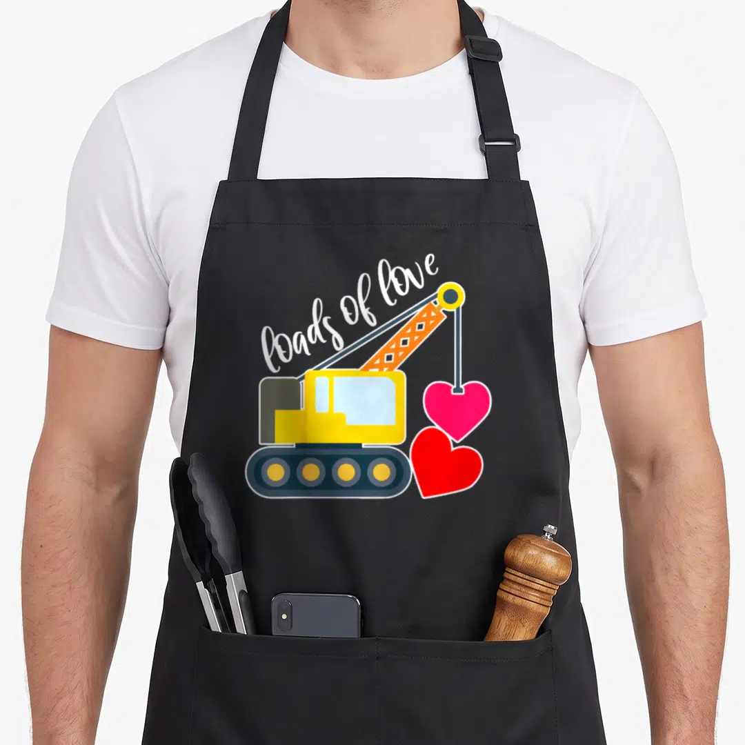Toddler valentine's day apron - Yellow crane lifting pink heart, red heart on ground, loads of love text in white script — shown on a black cotton canvas apron against a white background