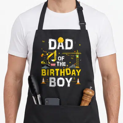 Cute birthday construction apron - Dad of the Birthday Boy text with excavator, crane, and construction cones in yellow — shown on a black cotton canvas apron against a white background