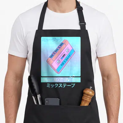 Mix 90s apron - Pink and blue cassette tape with Japanese text and MIX IT UP bar on grid background — shown on a black cotton canvas apron against a white background