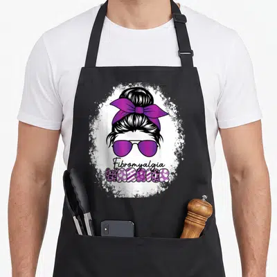 Cystic fibromyalgia awareness apron - Purple sunglasses woman bun Fibromyalgia Warrior text splatter background — shown on a black cotton canvas apron against a white background
