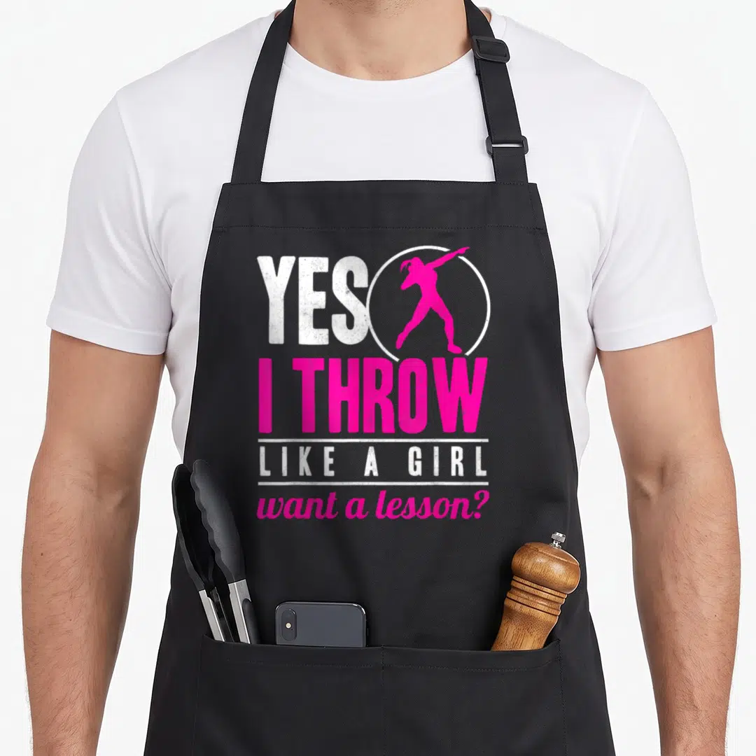 Throw track apron - Pink female athlete silhouette in white circle with Yes I Throw Like A Girl text — shown on a black cotton canvas apron against a white background