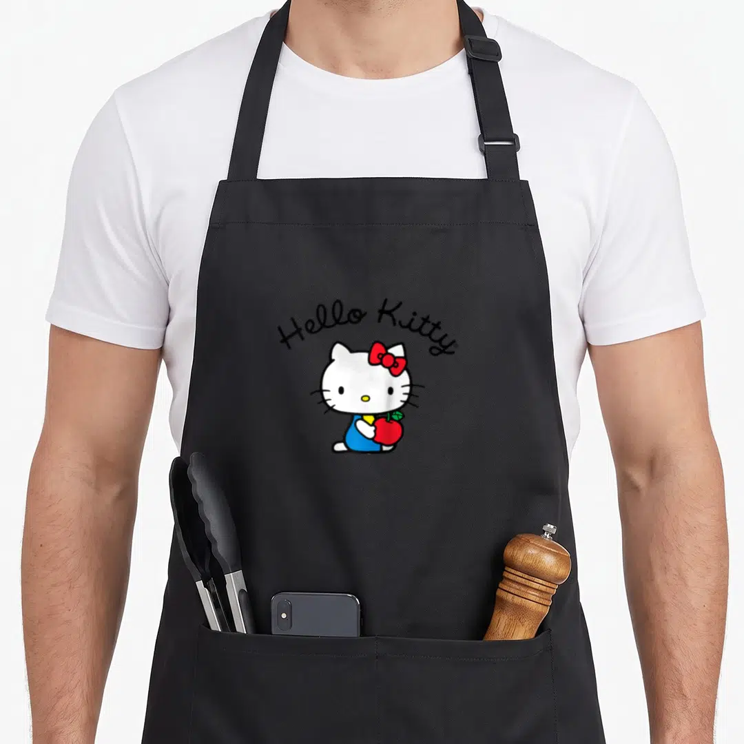 Funny baseball apron - Hello Kitty holding red apple with arched black text, white and blue details — shown on a black cotton canvas apron against a white background