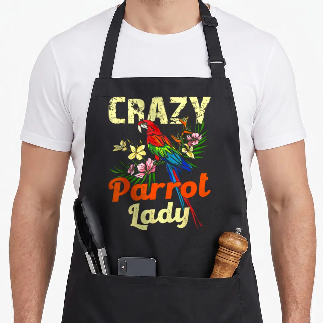 Birdwatcher animal apron - Cartoon parrot with red orange blue green feathers and tropical flowers under CRAZY Parrot — shown on a black cotton canvas apron against a white background