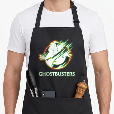 Funny neon ghost apron - Cartoon white ghost in circle with GHOSTBUSTERS text and motion lines — shown on a black cotton canvas apron against a white background