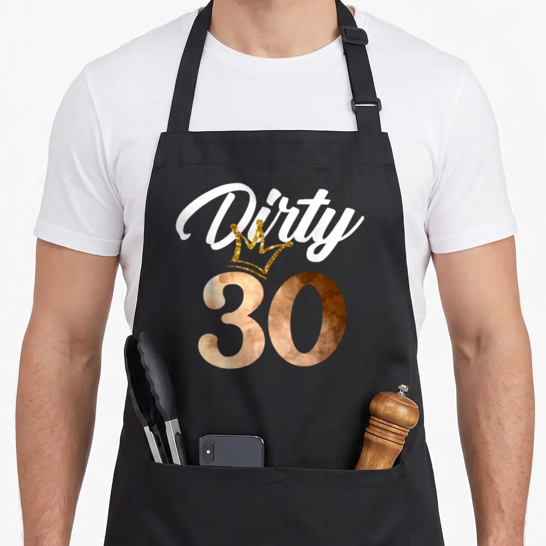 Crown funny dirty aprons - White Dirty script, gold crown, and rose gold 30 typography design — shown on a black cotton canvas apron against a white background