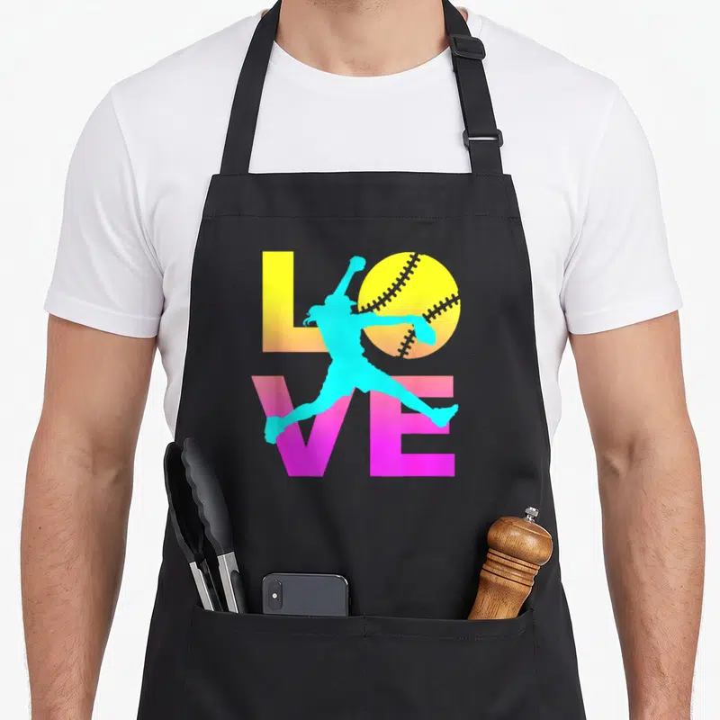 Retro softball apron - Cyan pitcher silhouette overlapping yellow LOVE text and stitched softball — shown on a black cotton canvas apron against a white background