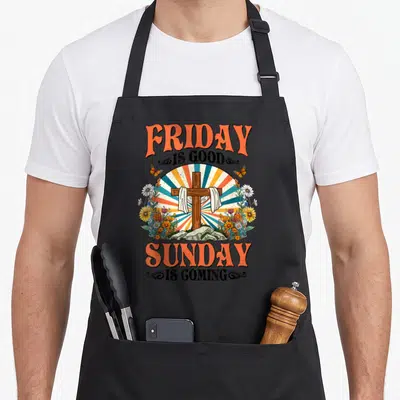 Coming easter apron - Retro cross with cloth, sunburst rays, flowers, and text Friday Is Good Sunday Is Coming — shown on a black cotton canvas apron against a white background