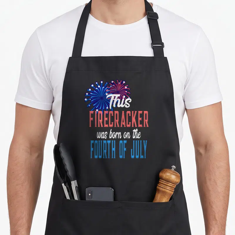 Firework 4th fourth of july aprons - Two red white and blue fireworks bursts above stacked text reading This — shown on a black cotton canvas apron against a white background