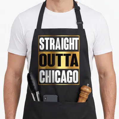 Outta chicago apron - Stacked text STRAIGHT OUTTA CHICAGO in white and black on gold and grey background within — shown on a black cotton canvas apron against a white background
