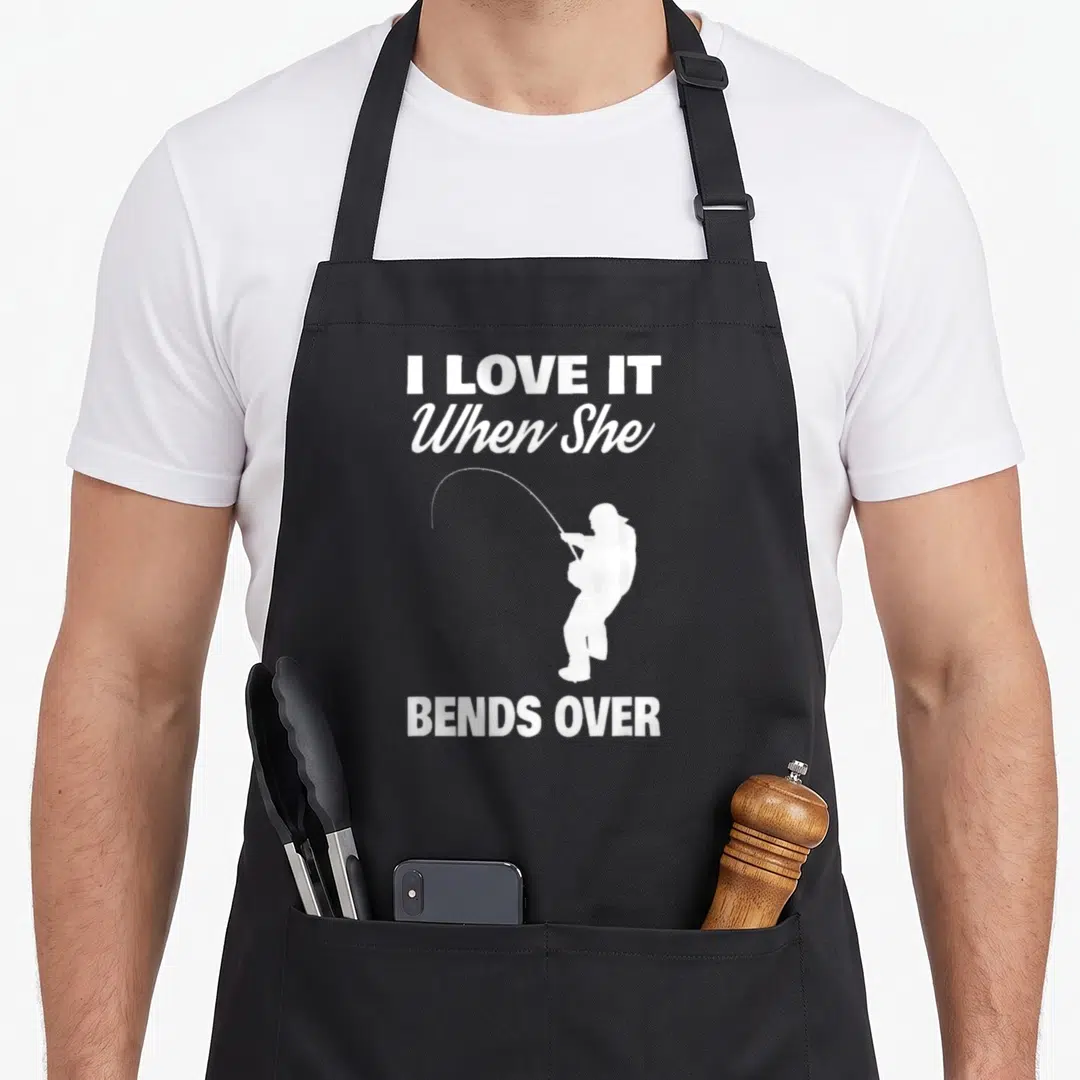 Vintage she fishing aprons - White text I Love It When She Bends Over with angler silhouette — shown on a black cotton canvas apron against a white background