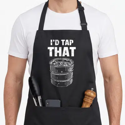 Tap bartender apron - White distressed text reading I'D TAP THAT above a line drawing of a beer keg — shown on a black cotton canvas apron against a white background