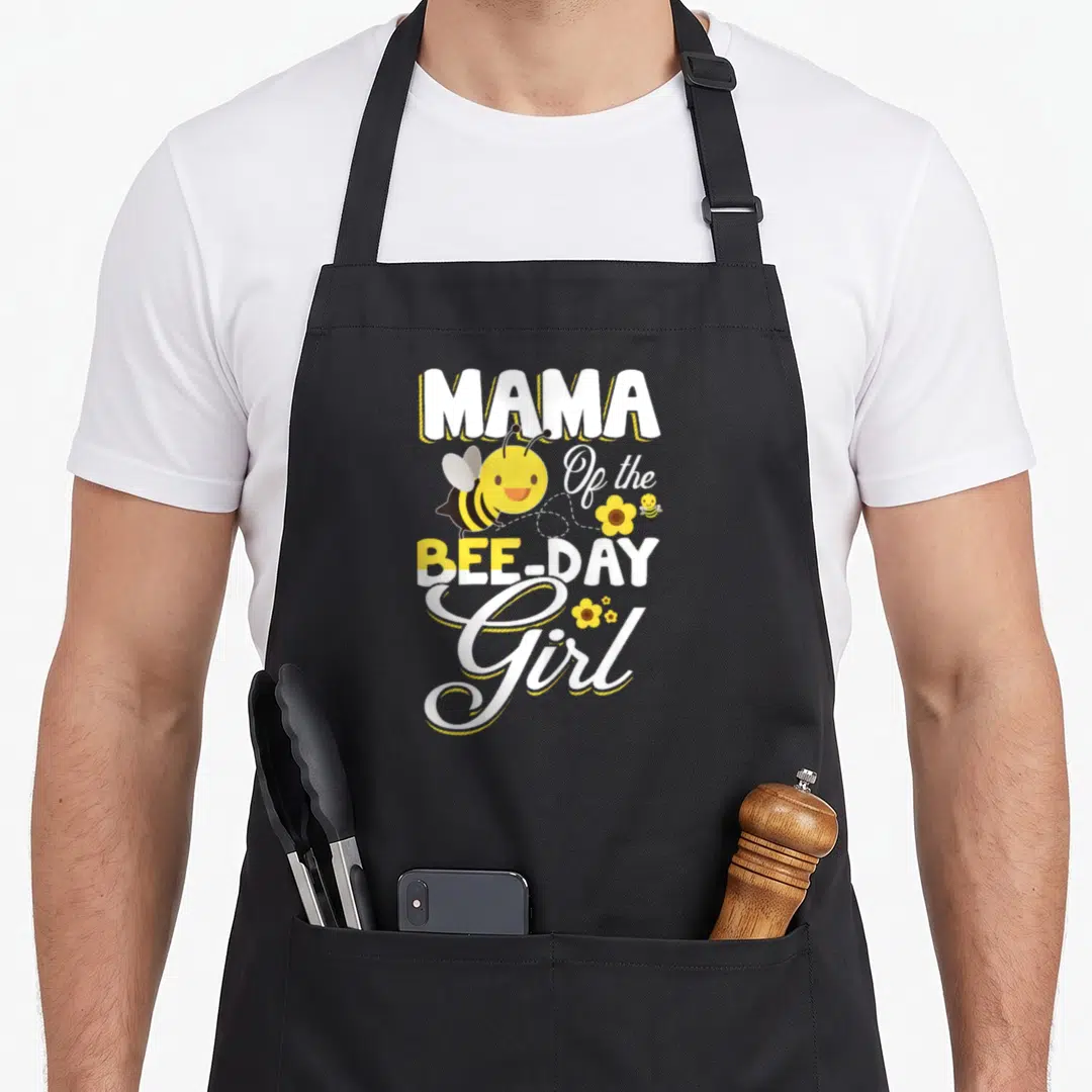 Mama bee aprons - Stacked Mama Bee Day Girl text with cartoon bees and yellow flowers — shown on a black cotton canvas apron against a white background