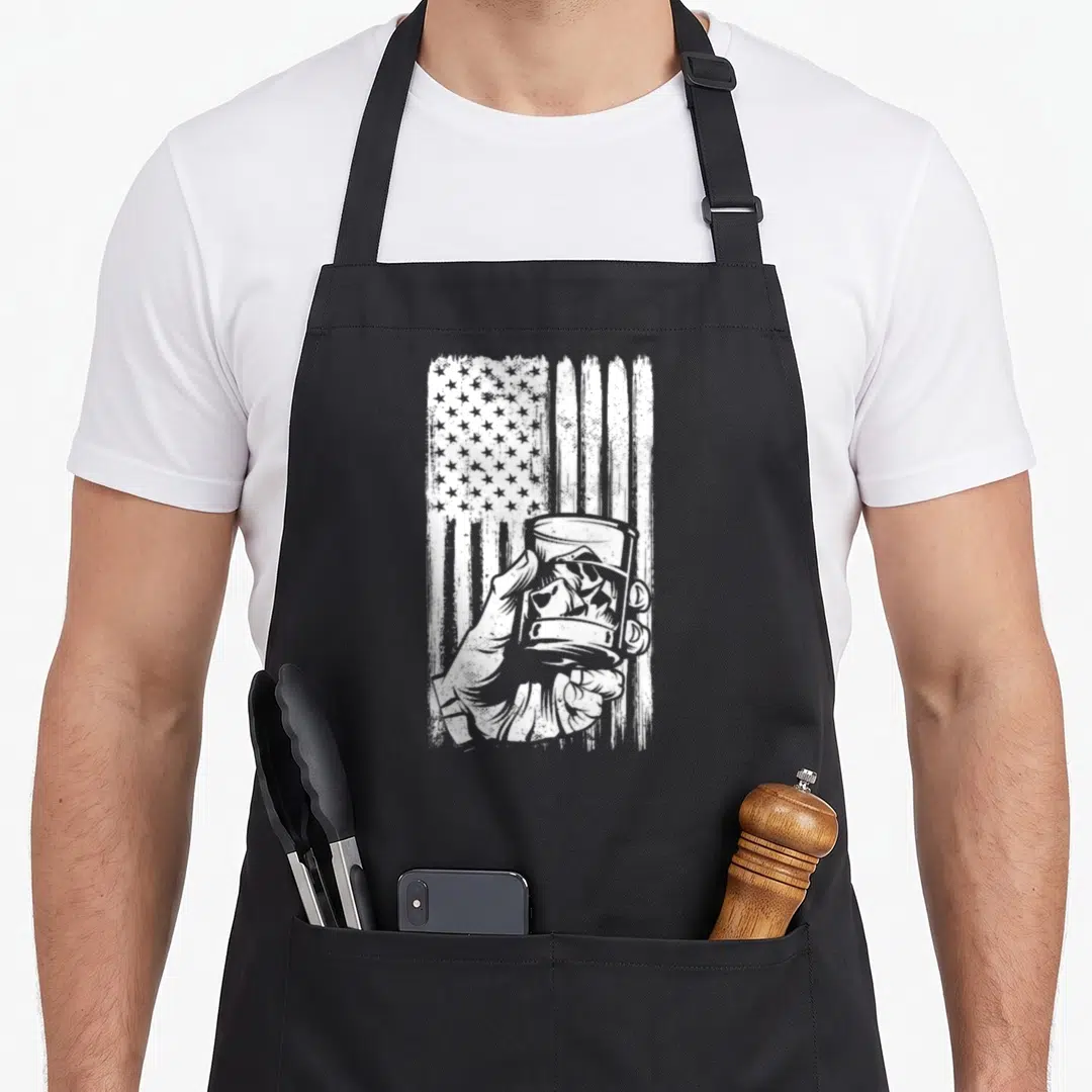 Scotch 4th of july apron - White hand holding ice glass over distressed American flag graphic — shown on a black cotton canvas apron against a white background