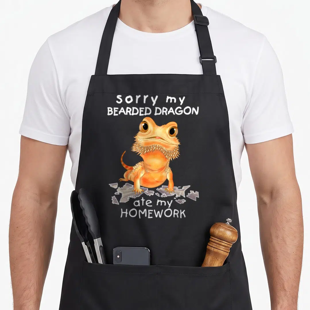 Lizard dragon apron - Orange cartoon bearded dragon standing on torn paper with white text — shown on a black cotton canvas apron against a white background