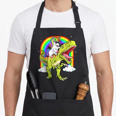 Rainbow unicorn dinosaur apron - Cartoon white unicorn with rainbow mane and sunglasses riding a green T-Rex — shown on a black cotton canvas apron against a white background