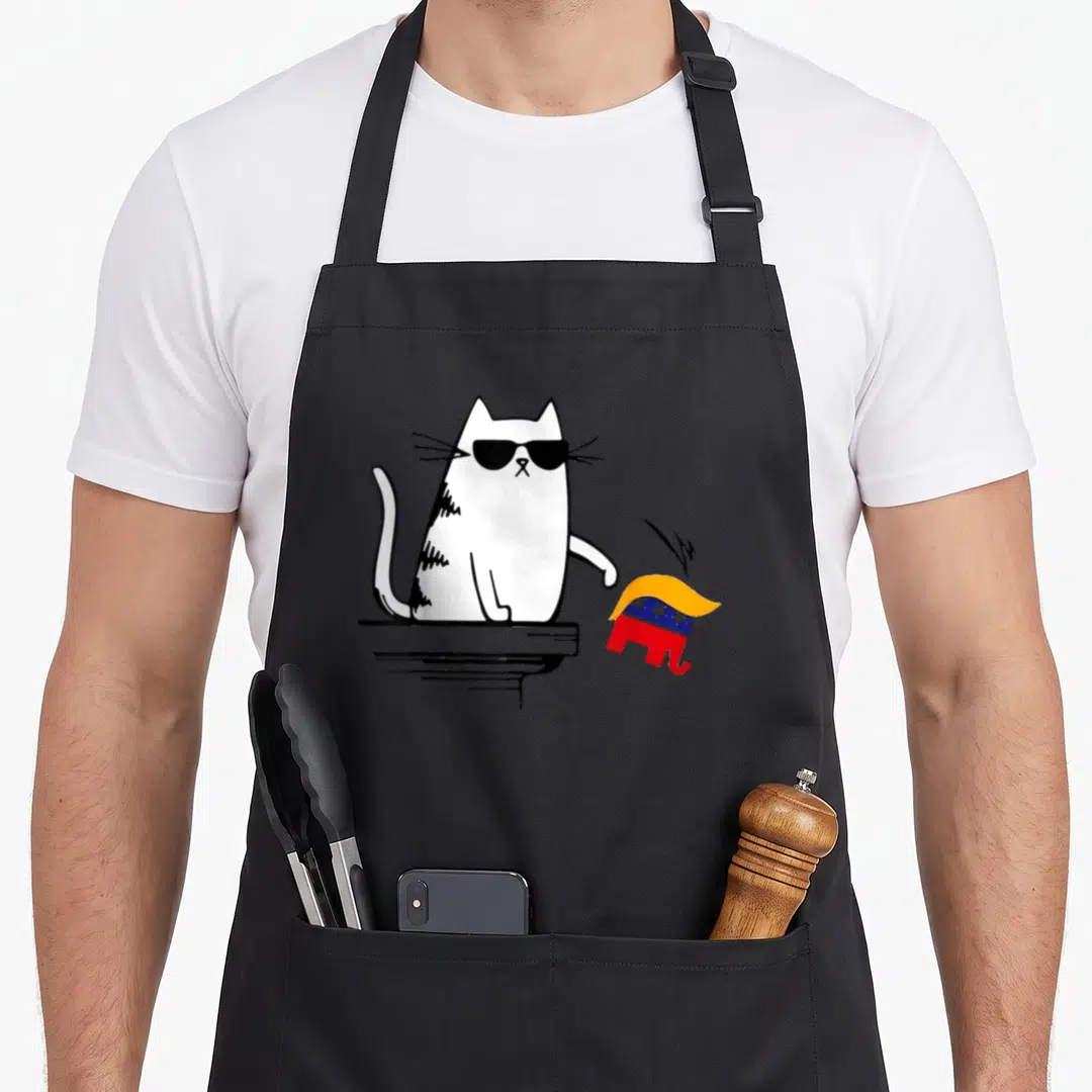 Cat elephant print apron - White cat with sunglasses knocking over red blue yellow elephant on black ledge — shown on a black cotton canvas apron against a white background
