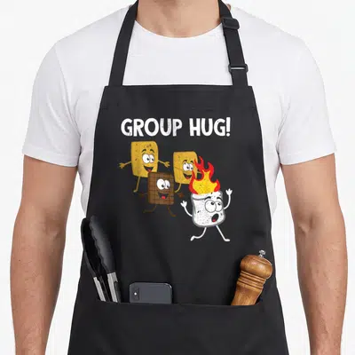 Smore food aprons - Cartoon marshmallow on fire running with crackers and chocolate under GROUP HUG text — shown on a black cotton canvas apron against a white background