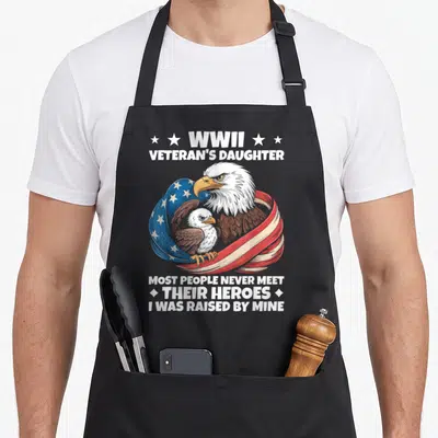 Daughter eagles apron - Bald eagle and chick wrapped in waving US flag with white text about WWII veteran daughter — shown on a black cotton canvas apron against a white background