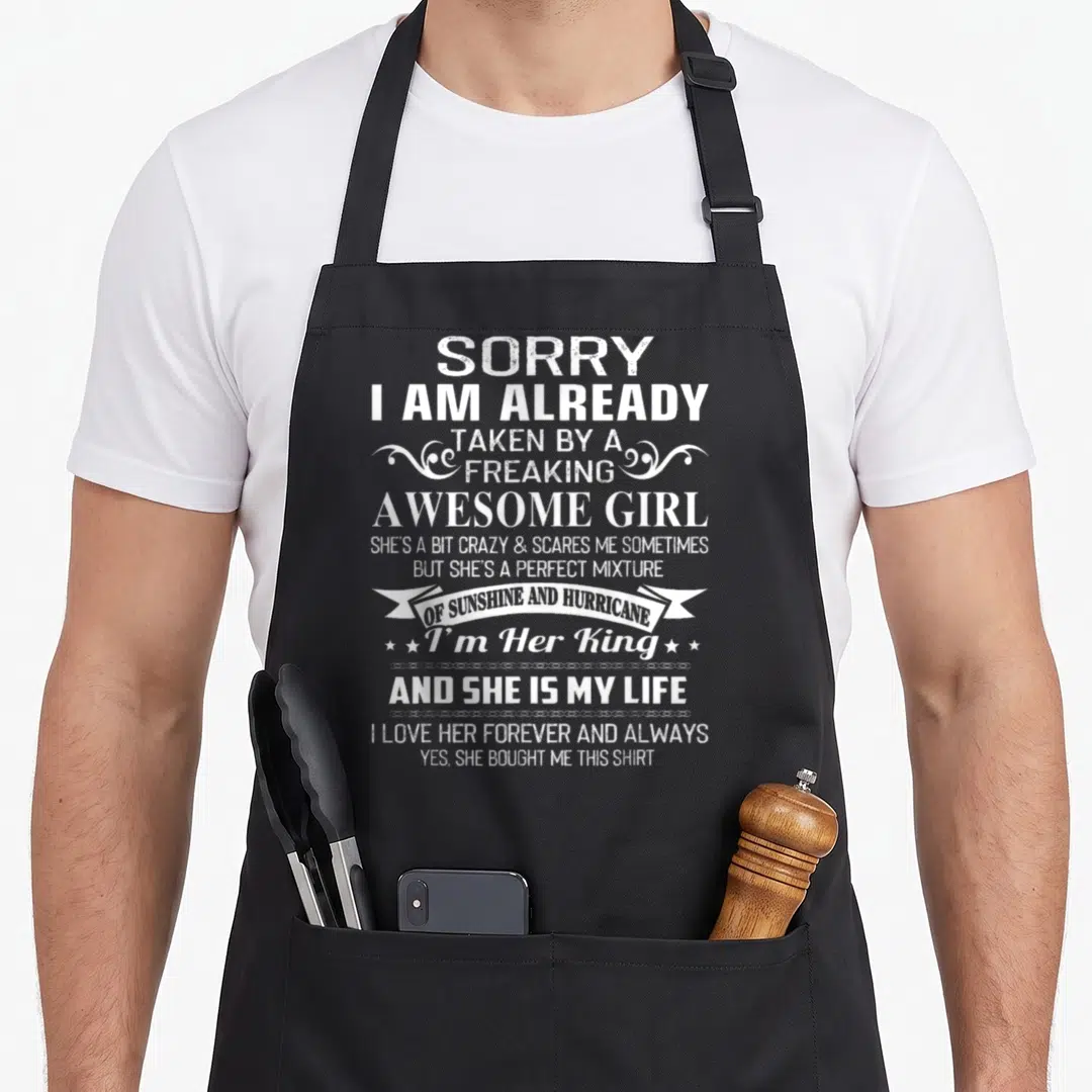 Already freaking apron - White distressed text quote about being taken by an awesome girl with banner and stars — shown on a black cotton canvas apron against a white background