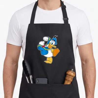 Ready steer apron - Cartoon Donald Duck in blue hat and yellow shoes on black fabric — shown on a black cotton canvas apron against a white background