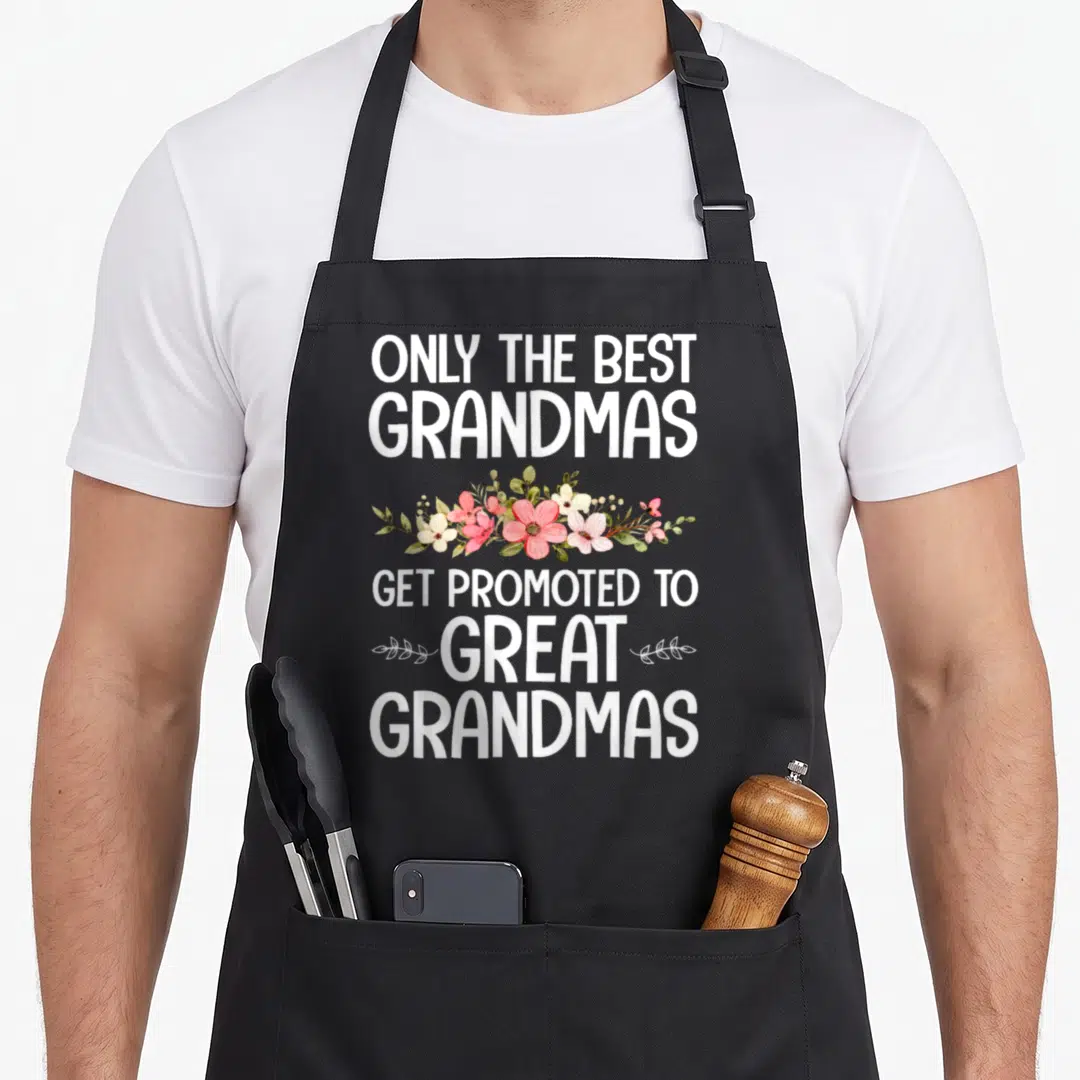 Funny grandmother grandma apron - White and pink watercolor flowers between text about best grandmas getting promoted — shown on a black cotton canvas apron against a white background