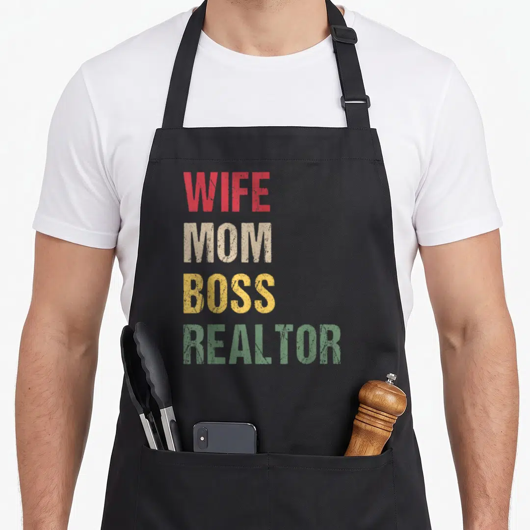 Boss wife apron - Stacked WIFE MOM BOSS REALTOR text in red beige yellow and green distressed fonts — shown on a black cotton canvas apron against a white background
