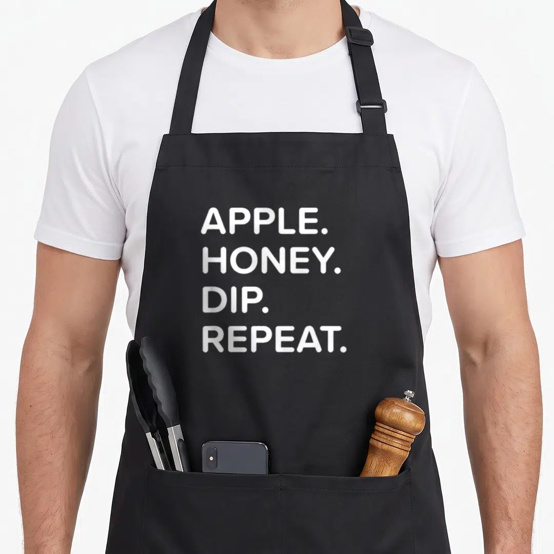 Rosh apple apron - White stacked text reading APPLE HONEY DIP REPEAT — shown on a black cotton canvas apron against a white background
