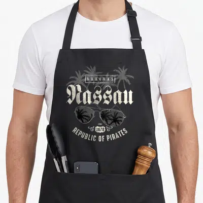 Nassau spring aprons - Retro Nassau text above sunglasses reflecting palm trees with Republic of Pirates below — shown on a black cotton canvas apron against a white background