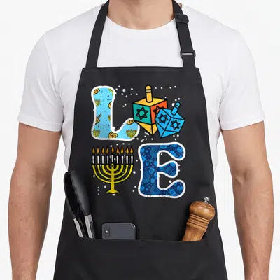 Menorah dreidel hanukkah apron - Cartoon LOVE text formed by a menorah, two dreidels, and patterned letters with white — shown on a black cotton canvas apron against a white background