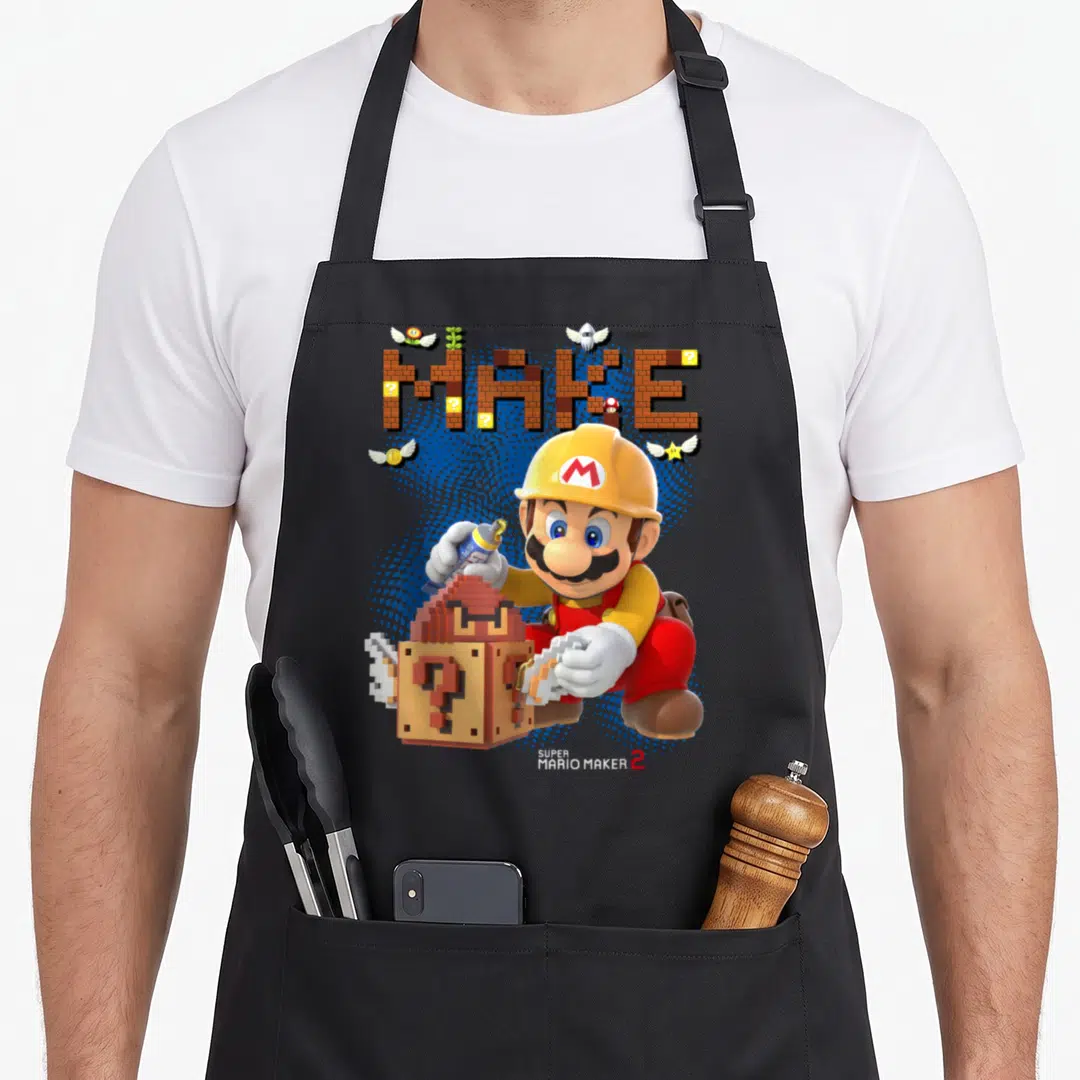 Block maker apron - Mario holding glue and block under brick MAKE text with game elements — shown on a black cotton canvas apron against a white background