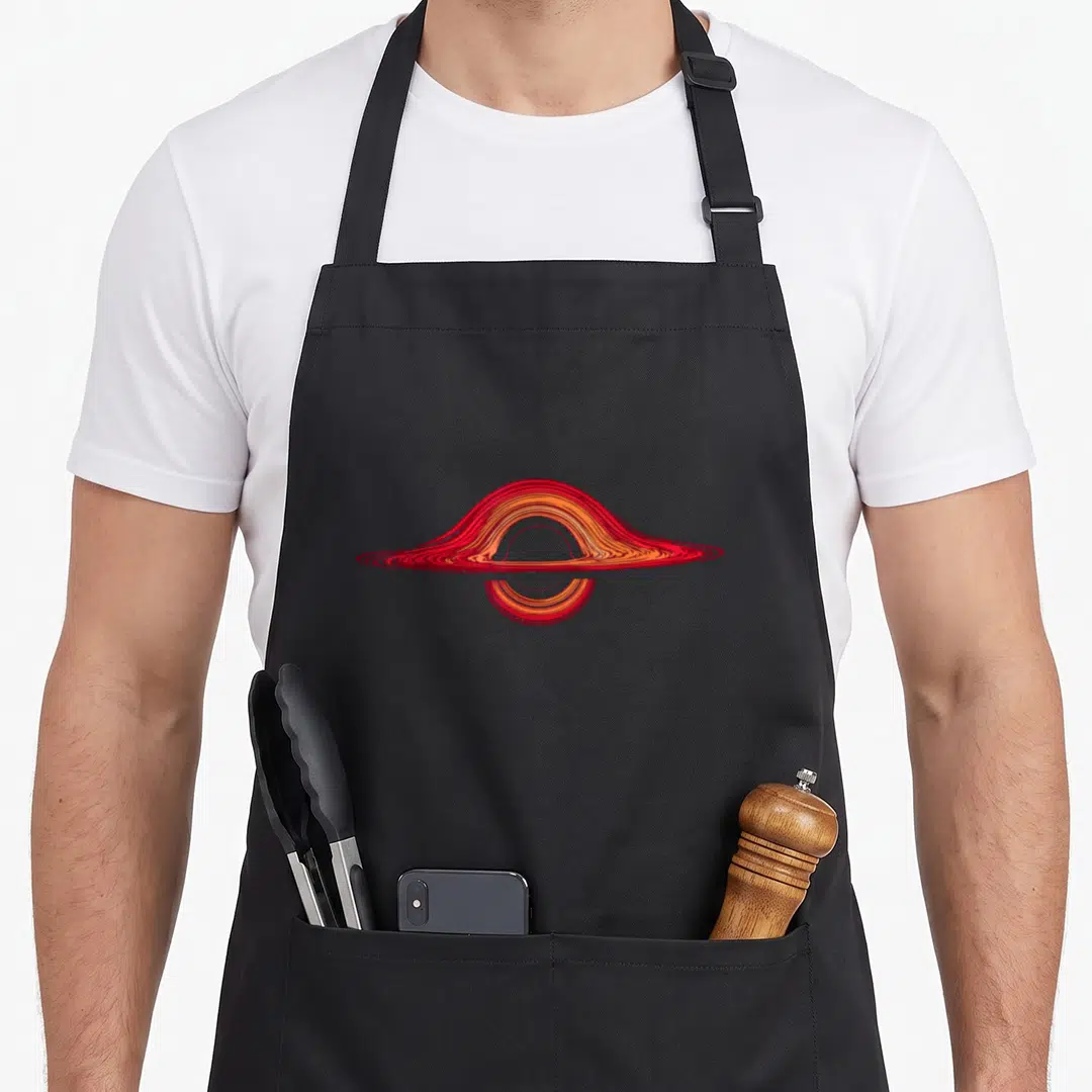 Hole astrophysicist apron - Stylized red and orange black hole accretion disk on grey background — shown on a black cotton canvas apron against a white background