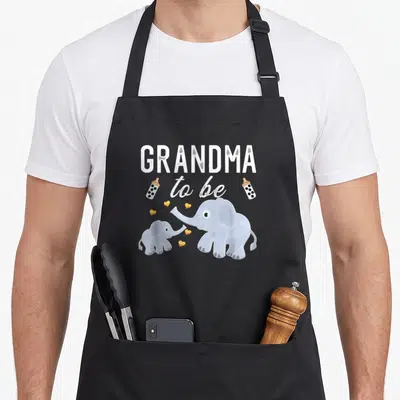 Elephant grandma apron - GREATMA to be text with two bottles and blue elephants facing each other among yellow hearts — shown on a black cotton canvas apron against a white background