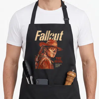 Ghoul tv apron - The Ghoul portrait with Fallout title and sarcastic quote in orange-red distressed print — shown on a black cotton canvas apron against a white background