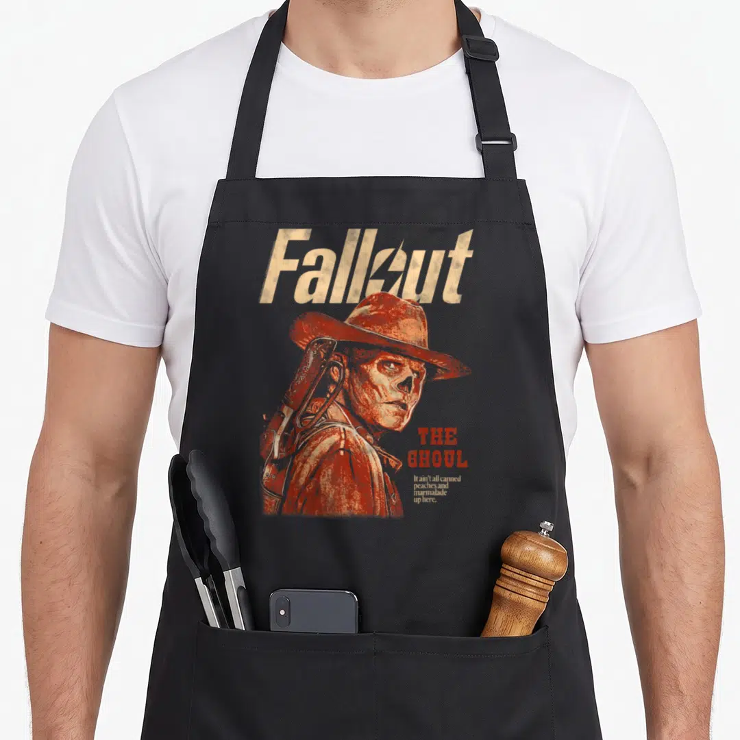 Ghoul tv apron - The Ghoul portrait with Fallout title and sarcastic quote in orange-red distressed print — shown on a black cotton canvas apron against a white background