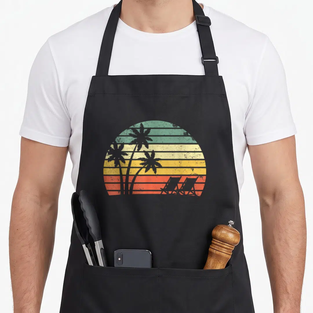 Chair tree apron - Retro sunset with teal yellow orange red bands, three palm trees, two beach chair silhouettes — shown on a black cotton canvas apron against a white background