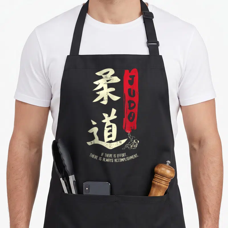 Japanese judo apron - White Kanji characters next to a red vertical JUDO brush stroke with two small line-art figures — shown on a black cotton canvas apron against a white background