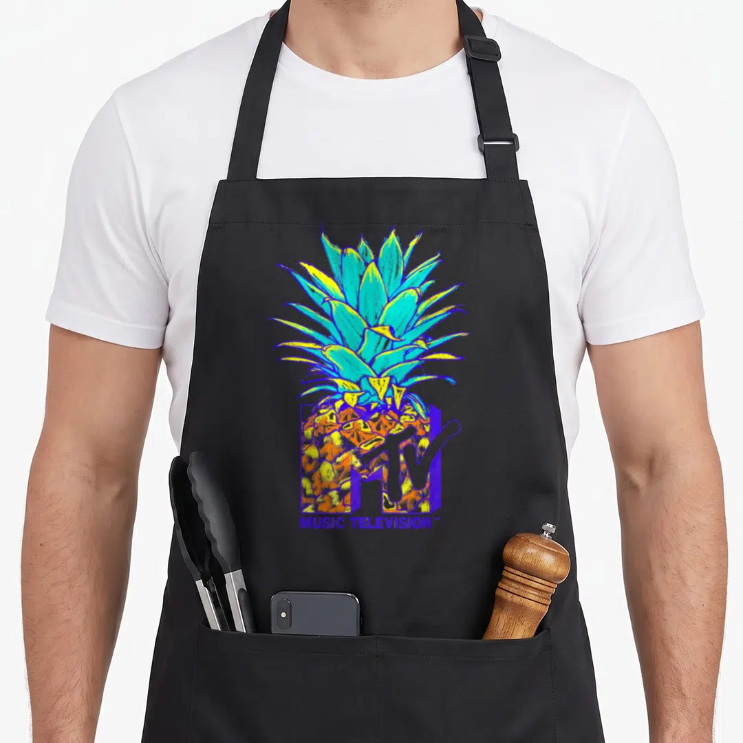 Mtv pineapple apron - Colorful cartoon pineapple behind purple MTV logo with MUSIC TELEVISION text below — shown on a black cotton canvas apron against a white background
