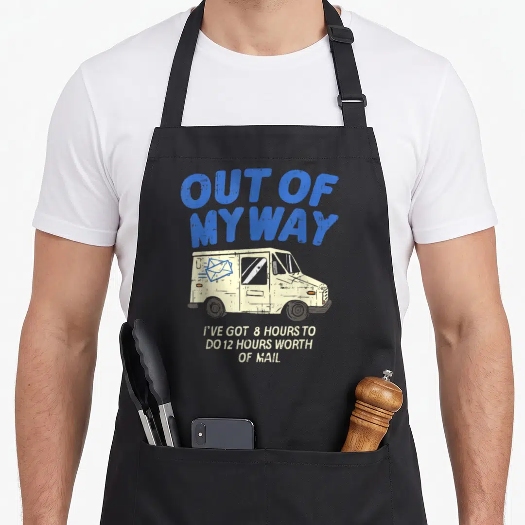 Postal truck apron - Arched blue text OUT OF MY WAY above beige mail truck with stacked caption about 8 hour shift — shown on a black cotton canvas apron against a white background