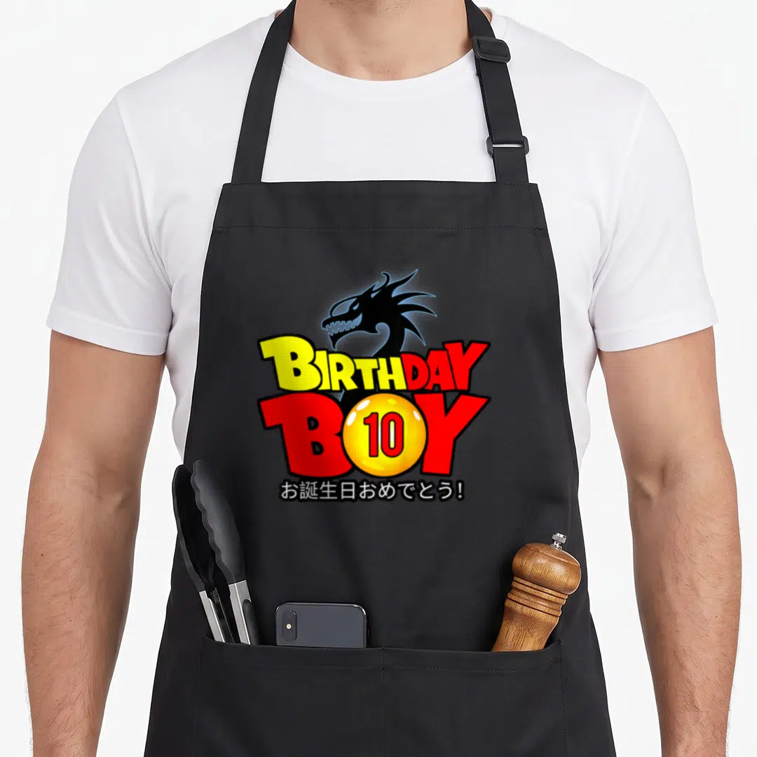 10th anime mom apron - Black dragon head above stacked BIRTHDAY BOY text with yellow 10 ball and Japanese greeting — shown on a black cotton canvas apron against a white background