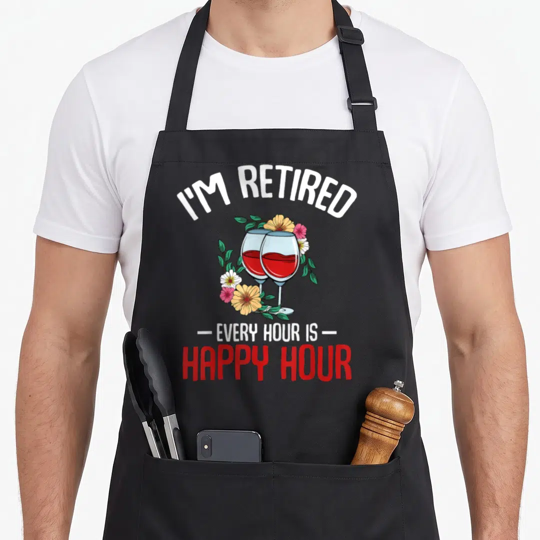 Hour retiree apron - Two wine glasses with red liquid surrounded by yellow, green, white, and pink flowers — shown on a black cotton canvas apron against a white background