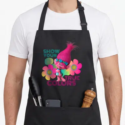 Show troll apron - Pink cartoon character flanked by flowers with Show Your True Colors text — shown on a black cotton canvas apron against a white background