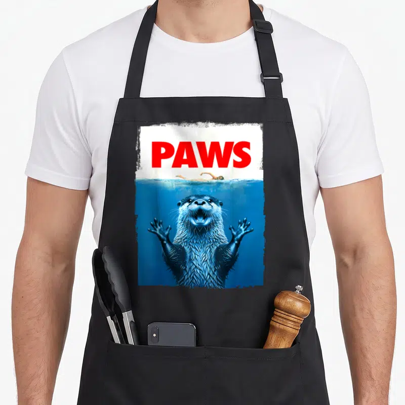 Paw otter mom apron - PAWS text above swimmer and underwater otter in blue and red — shown on a black cotton canvas apron against a white background