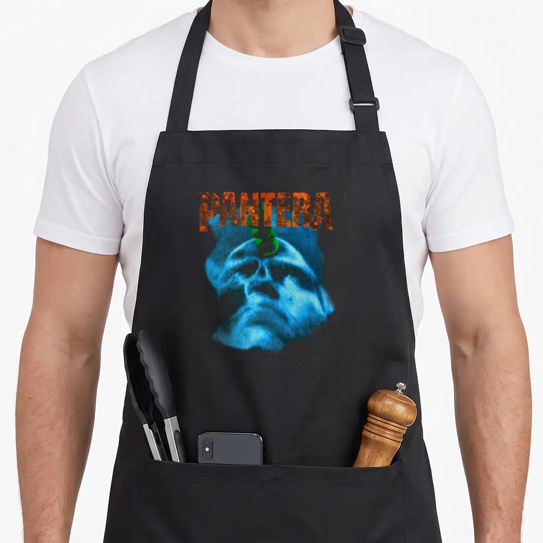 Driven beyond apron - Distressed orange PANTERA text above a blue horned skull with green accents — shown on a black cotton canvas apron against a white background
