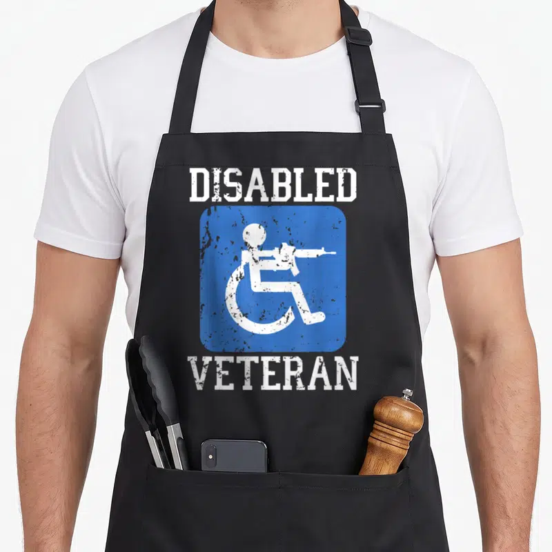 Disabled military apron - Blue square with white wheelchair user holding rifle, DISABLED VETERAN text above and below — shown on a black cotton canvas apron against a white background