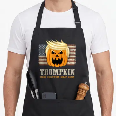 Flag halloween apron - Blonde pumpkin on distressed flag with TRUMPKIN text — shown on a black cotton canvas apron against a white background