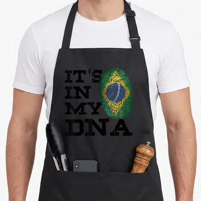 Dna brazilian apron - Distressed IT'S IN MY DNA text beside a fingerprint shaped like the Brazilian flag in green — shown on a black cotton canvas apron against a white background