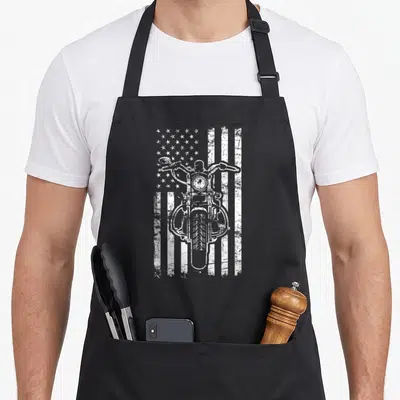 Biker patriotic aprons - White distressed motorcycle front view over American flag stripes and stars — shown on a black cotton canvas apron against a white background