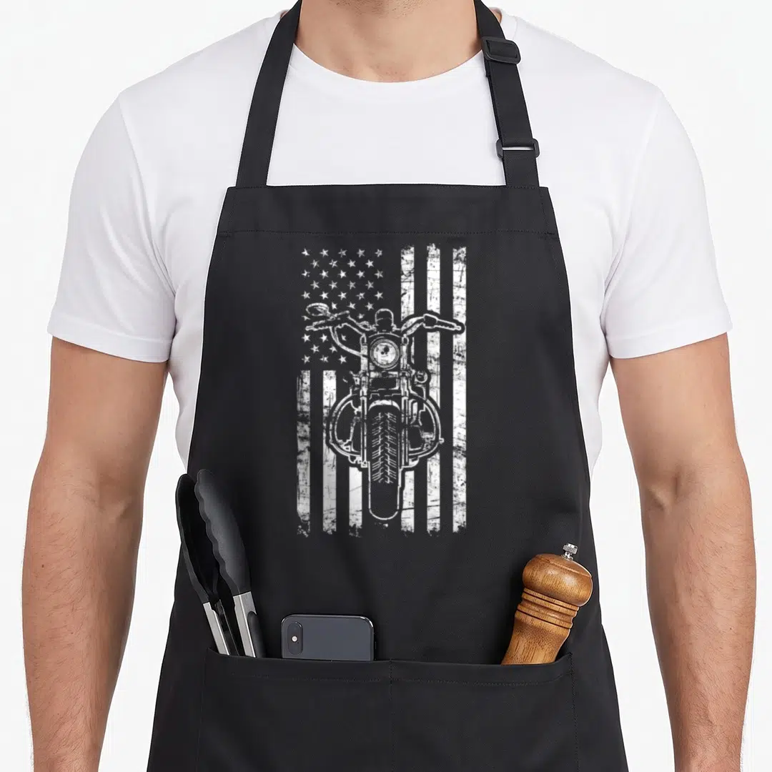 Biker patriotic aprons - White distressed motorcycle front view over American flag stripes and stars — shown on a black cotton canvas apron against a white background