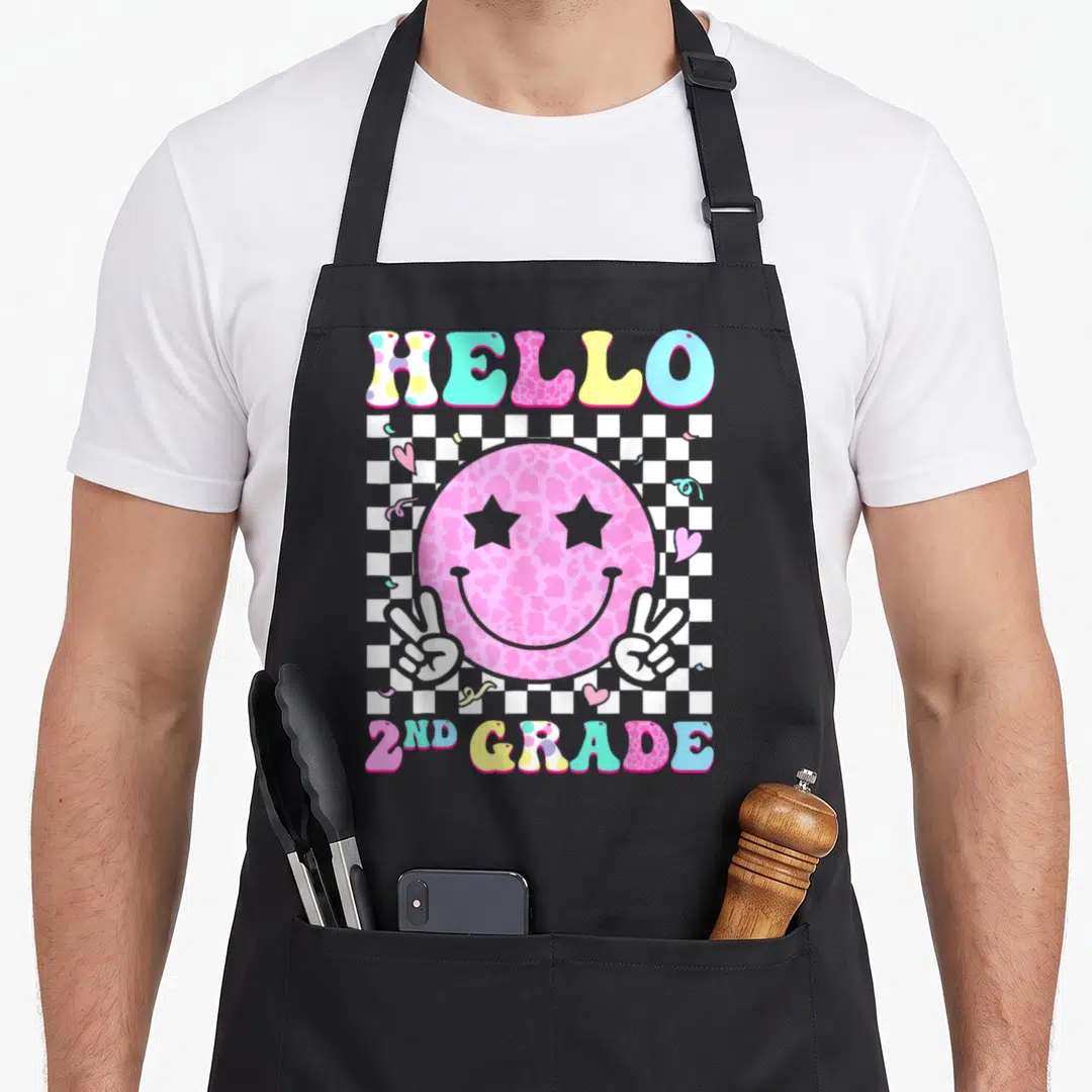 Hello grade 2nd apron - Pink smiley face with star eyes on checkerboard with peace signs hearts confetti and HELLO 2ND — shown on a black cotton canvas apron against a white background